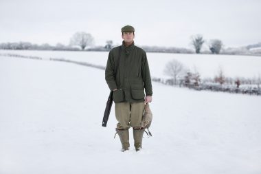 A man standing in a snow covered field in Salisbury with a dead pheasant and a shotgun with his eyes closed.