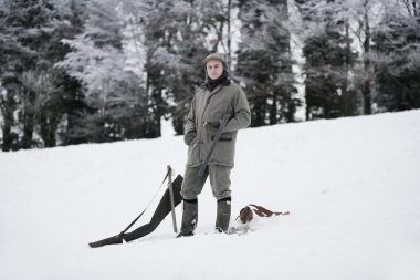 A man with his eyes closed with a shotgun in a field of snow.