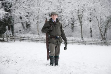 A man in the snow with a shotgun and cartridges.