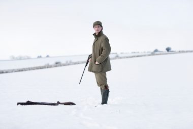A man with a shotgun with his eyes closed in a field of snow.