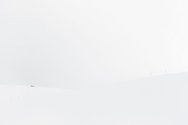 A barely visible hut on a ski slope in Norway with coloured poles visible