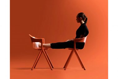 A woman sat oin an orange chair in a studio phoptograph