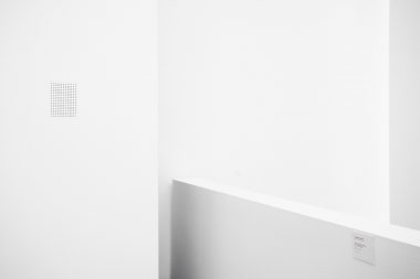 A speaker in a white gallery wall with an information panel about a sound piece in MACBA, Barcelona.
