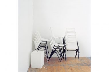 White and black chairs stacked in the corner of a white art studio.