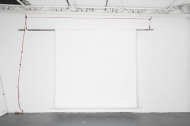 A white roll of background paper hanging against a white wall with a red rope in a photography studio.