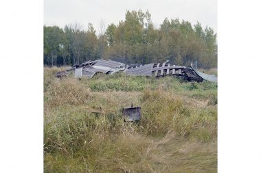 A dilapidated house in a field with a warning sign in the foreground.