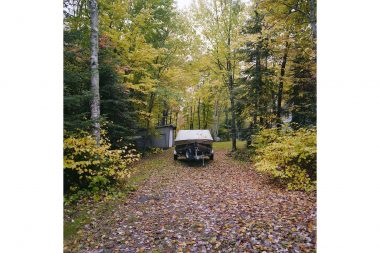 A speedboat under a cover surrounded by autumnal trees.