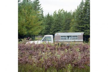 The side of a caravan vehicle at the edge of a forest.