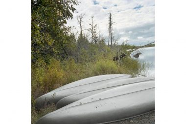 Three metal kayaks by a lake in Minnesota with trees in the background.