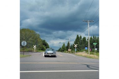 A car waiting at a junction with a dark sky in the background.