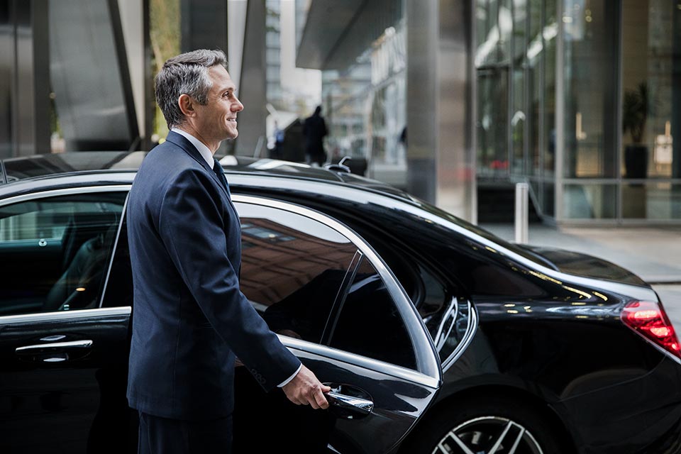 Driver with Mercedes welcoming his passengers using the London chauffeur service.