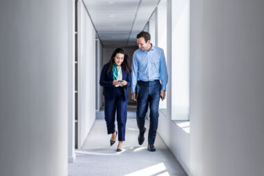 A man and a woman walking down a corridor in a corporate office building.