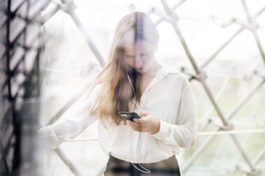 A woman making a call on a mobile with headphones in a corporate building.