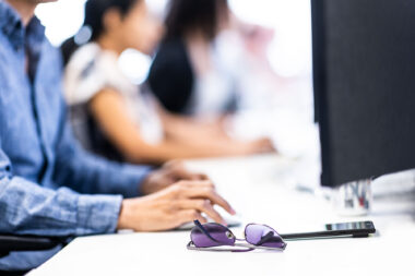 A corporate lifestyle photograph of people working at computers with sunglasses in the foreground.