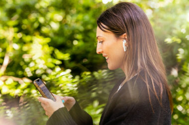 A woman with a phone on a call with trees in the background.