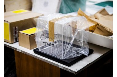 An empty display case wrapped in plastic with the name of Gavin Turk written on it.