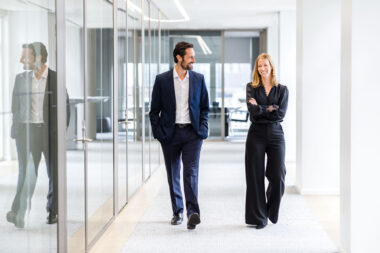 A corporate lifestyle photograph of a man and a woman walking down a corridor in an office space.