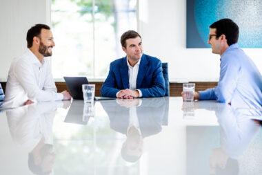 Corporate lifestyle photograph of three men having a meeting around a table.