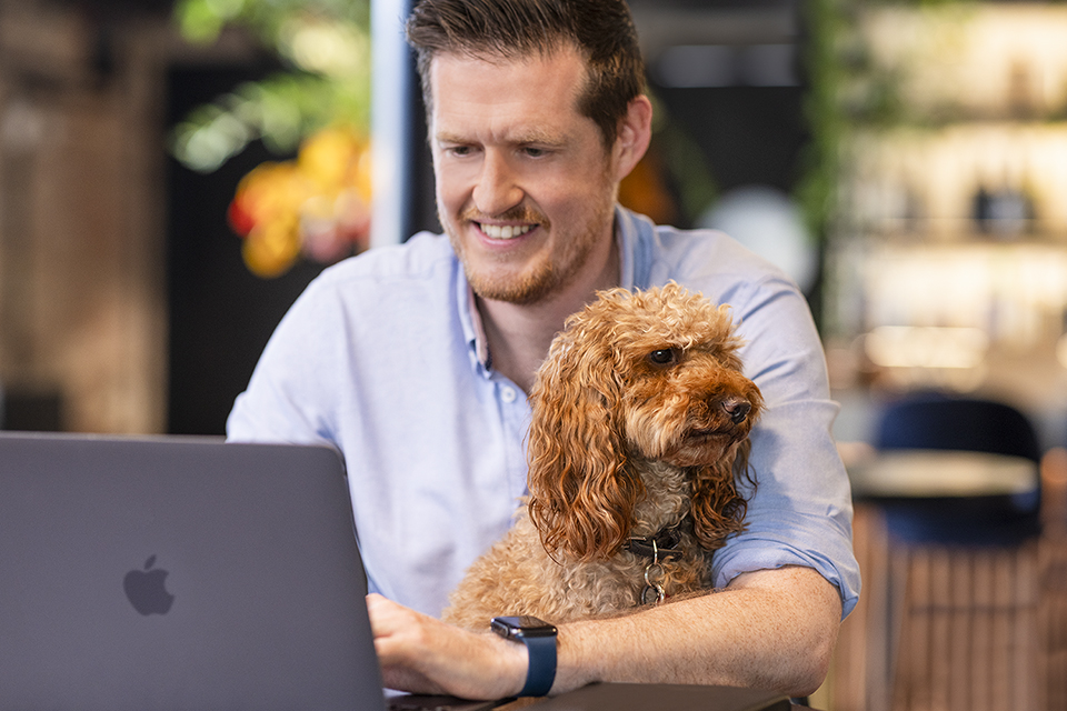 A man working on a laptop with a dog at a London office. Image by Richard Boll Photography.