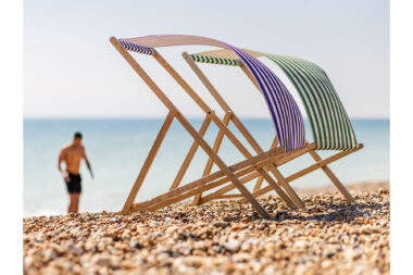 A man on a beach with deckchairs in the foreground.