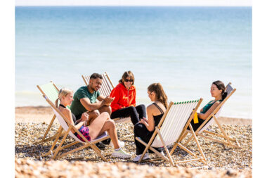 A group of friends sat on deckchairs on the beach.
