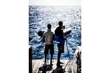 Two men standing on the deck of a diving liveaboard boat looking out to sea - candid authentic lifestyle photographer.