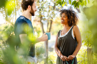 A woman chatting while leaning on a garden fork in an allotment and a man with a cup of tea- intimate and authentic lifestyle photography.