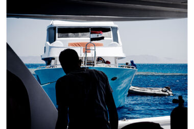 The back of a man working on a liveaboard diving boat in the Red Sea in Egypt, looking towards another diving boat- authentic diving lifestyle photography from Richard Boll.