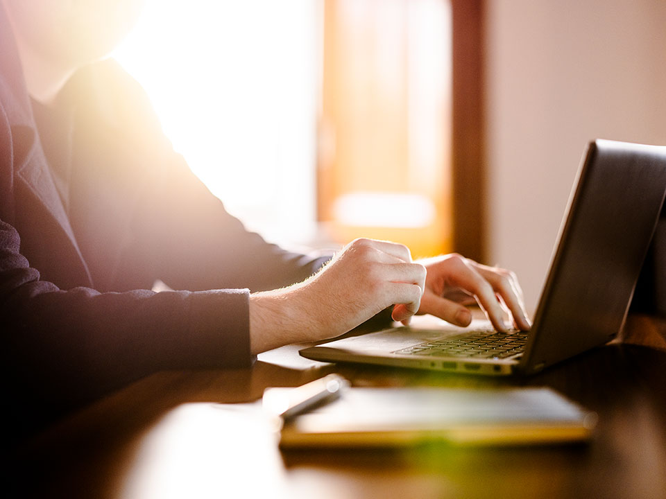 A man at a laptop in evening light photographed by Richard Boll for Rathbones.