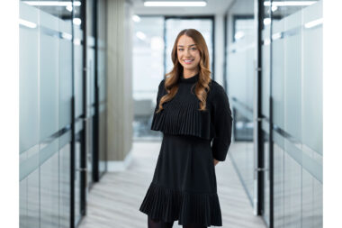A corporate portrait of a woman standing in a glass corridor in London.