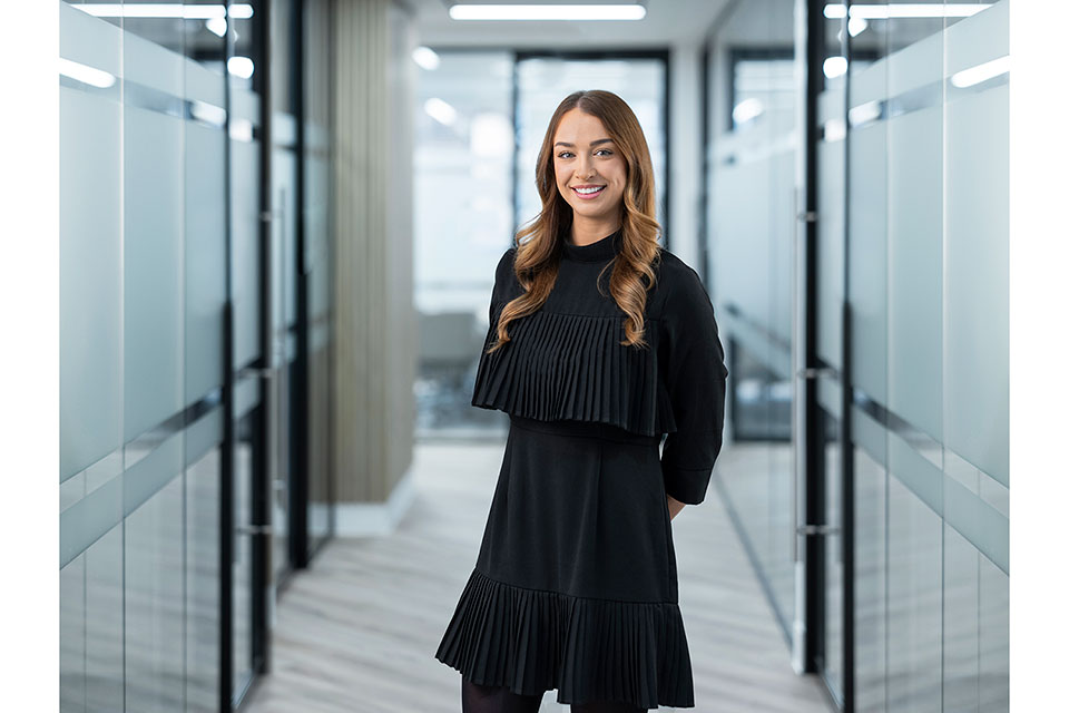 A corporate shoot at a London office. Glass-walled meeting spaces are on either side of the member of staff, who is dressed all in black. Image by Richard Boll.