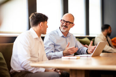 Two men talking whilst working with a laptop in a modern co-working space.